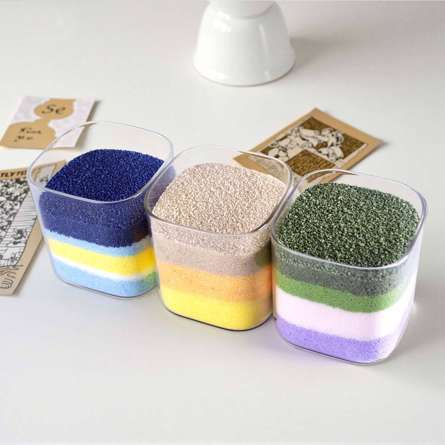 Three clear glass vessels filled with layers of colored candle sand granules