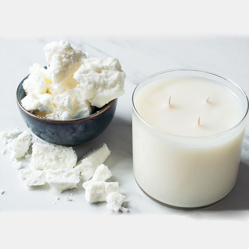 Chunks of white coconut apricot wax in a dark bowl beside a poured container candle
