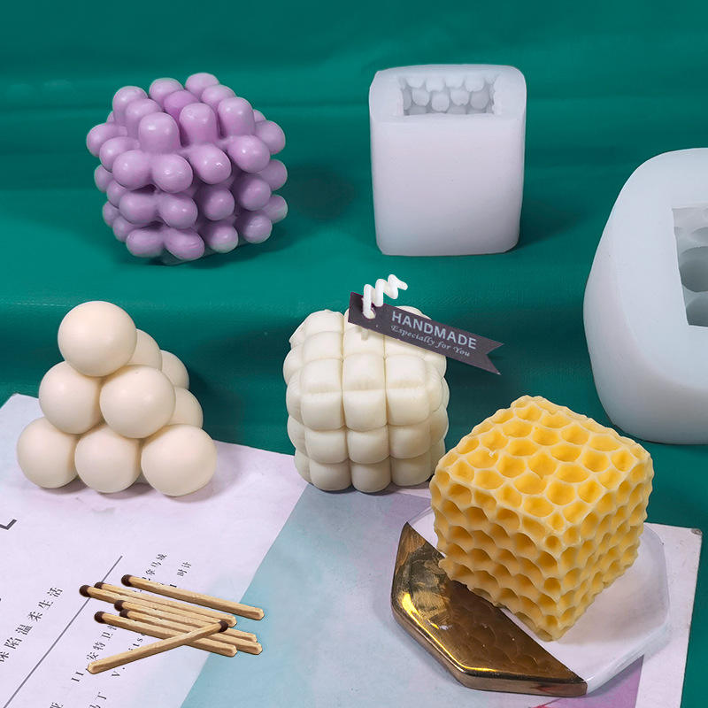 A white silicone candle mold beside cast candles in bubble, cube and honeycomb shapes